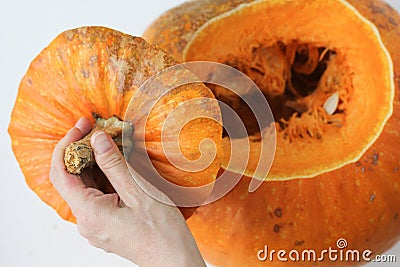 Whole pumpkin after several minutes in oven and woman hands holding cutted top of pumpkin on the white background. Concept how to Stock Photo