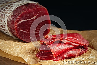 Whole and sliced bresaola on paper on a cutting board Stock Photo