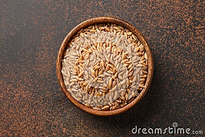 Wholegrain spelt farro in wooden bowl on brown background. Top view Stock Photo