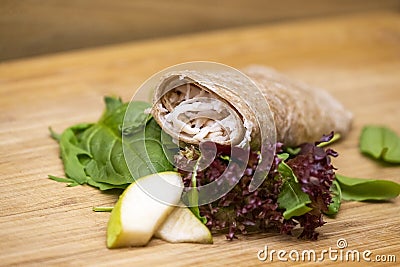 Wholemeal wrap with goat cheese, pear and salad. Fresh healthy food, snack on wooden background Stock Photo