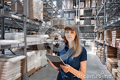 Wholesale warehouse. Beautiful young woman worker of store in shopping center. Girl looking for goods with a tablet is Stock Photo