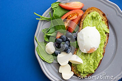 Wholesome tasty full of vitamins and health breakfast with avocado, berries, cheese and tomatoes with basil. Stock Photo
