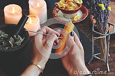 Wiccan witch carving symbols and sigils onto yellow gold color candlestick at her altar Stock Photo