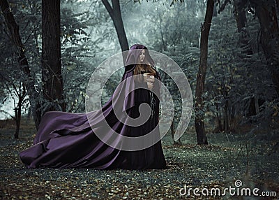 Wicked witch in a long dark cloak wandering in woods Stock Photo