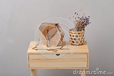 a wicker bag with handles in brown chains with dry plants stands on a brown wooden table Stock Photo
