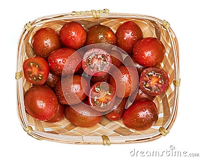 Wicker basket with cherry tomatoes mini kumakos cut in half and whole. With drops of water. Stock Photo