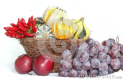 Wicker basket with gourd pumpkins, blue grapes, apples and Chili Stock Photo