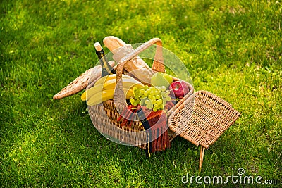 Wicker picnic basket with fresh fruits, wine bottle, baguette and plaid on green meadow Stock Photo