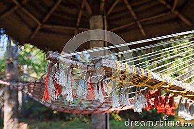 A wicker suspended summer chair hangs in the shade of tropical trees. Stock Photo