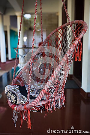 A wicker suspended summer chair hangs in the shade of tropical trees. Stock Photo