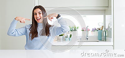 Wide angle picture of beautiful young woman sitting on white table at home smiling confident showing and pointing with fingers Stock Photo