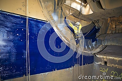 Rope access painter working at height hanging on twin ropes wearing safety harness chemical mask commencing spray painting in conf Stock Photo