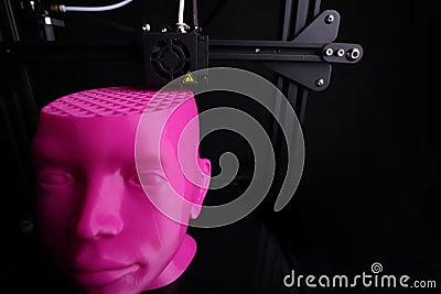 Wide angle view on a 3D printer manufacturing a humanoid head from pink plastic in dark light Stock Photo