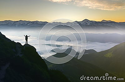Wide mountain panorama. Small silhouette of tourist with backpack on rocky mountain slope with raised hands over valley covered Stock Photo
