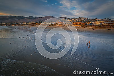 Wide sandy beach with people, Pacific ocean, hills, and cloudy sky. Pismo Beach at sunset, California coastline Editorial Stock Photo