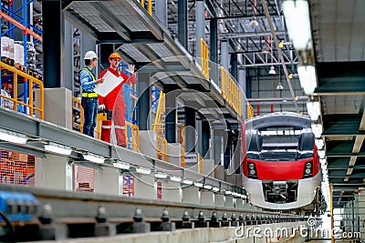 Wide shot of engineer hold drawing plan and technician worker stay and discuss beside railroad tracks of electrical or sky train Stock Photo
