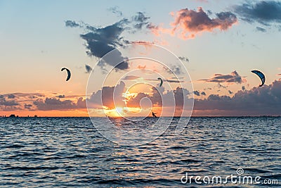 Wide shot of three kitesurfers riding in sunset conditions with colorful clouds in the sky Stock Photo