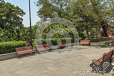 Wide view of group of unoccupied wooden seats or chairs arranged in a garden or park, Chennai, India, April 1st 2017 Editorial Stock Photo