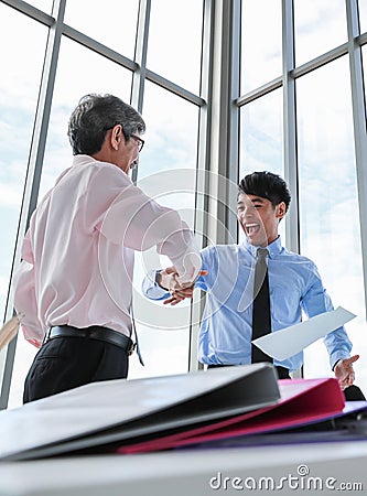 Wide view shot of two Asian businessmen looking at each other eyes with a pleasant smiling and shaking hands. The senior and young Stock Photo