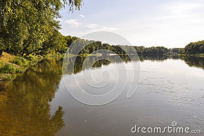 Wide yellow river is slow flowing. Early autumn. Sunny weather and brightgreen trees on the banks fron the both sides Stock Photo