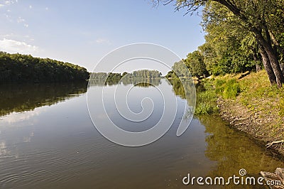 Wide yellow river is slow flowing. Early autumn. Sunny weather and brightgreen trees on the banks fron the both sides Stock Photo