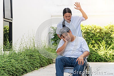 The wife was pushing the wheelchair for her husband. With her raised hands pretending to hit him. Because of being bored with her Stock Photo