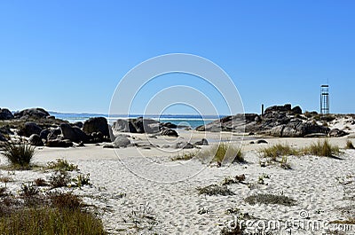 Wild beach with vegetation in the sand, rocks, turquoise water with waves and lifeguard tower. Galicia, Spain. Sunny day, blue sky Stock Photo