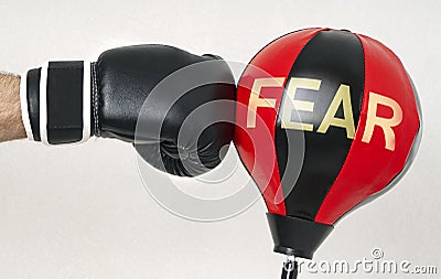 Win the fear concept with a strong man`s hand in a boxing glove hits the punching bag with text Fear Stock Photo