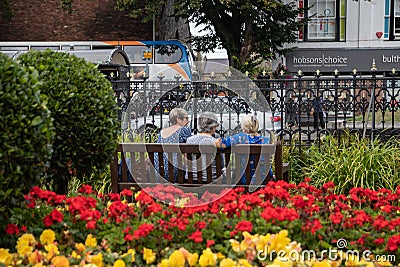 Three middle aged women sat on a wooden bench in the park surrounded by flowers Editorial Stock Photo