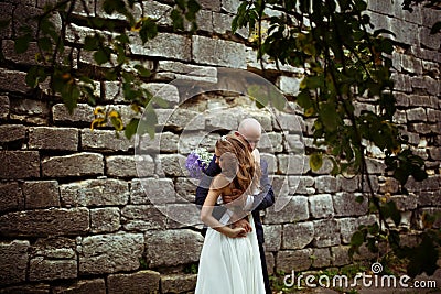 Wind blows away bride's hair while groom hugs her under the tree Stock Photo