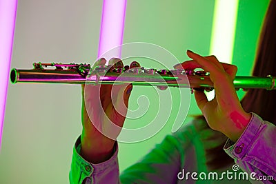 Wind instrument flute close up. Female hands hold a flute against the background of bright neon lights in a dark studio Stock Photo