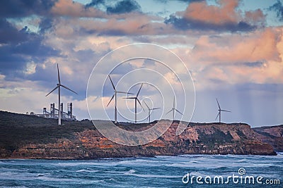 Wind turbines standing on rugged cliff above ocean in Australia at sunset. Stock Photo