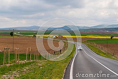 A winding country road, plowed fields, canola fields, and mountains in background Stock Photo