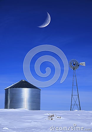 Windmill and Grain Silos in Winter Snow on Farm for Agricultural Farming with Crescent Moon Stock Photo