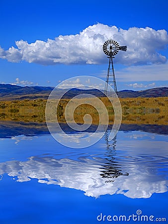 Windmill on Hillside in Countryside Rural America with Sky and Clouds Reflection in Water Pond Lake Reflect Stock Photo