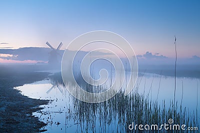 Windmill by river in misty dusk Stock Photo