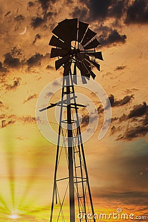 A windmill silhouette at sunset with the sun and moon and cloudy sky Stock Photo