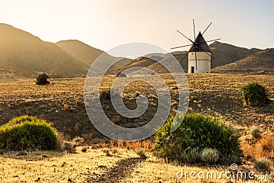 Windmill at sunset between the hills. Light and golden fields in southern Spain. Stock Photo