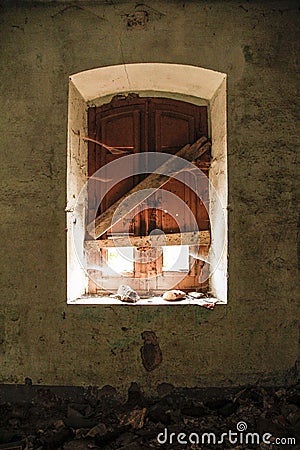 Window of an abandoned house taken from inside; the light illuminates the room a little, leaving a glimpse of the cobwebs and the Stock Photo