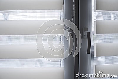 Window handle and white fabric roller blinds on the white plastic window in the living room. Close up on roll curtains Stock Photo