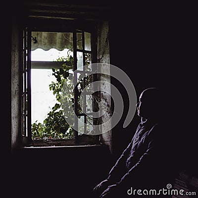 Window view from inside an old uninhabitable house and a blurred silhouette of a man. Depression, loneliness, despair, decline, Stock Photo