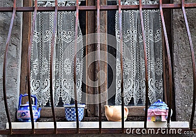 Window with white embroidery curtains and with colored ceramic objects on the windowsill in the ancient part of San Romano in Garf Stock Photo