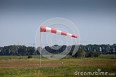 Windsock, weather vane for airfields. Red and white striped fabric showing wind speed, strength and direction. Umbrella cap at the Editorial Stock Photo