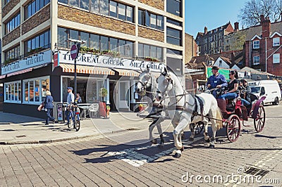 Tourists enjoying a sightseeing tour by a vintage hackney carriage drawn by white horses in the town of Windsor in Berkshire, UK Editorial Stock Photo