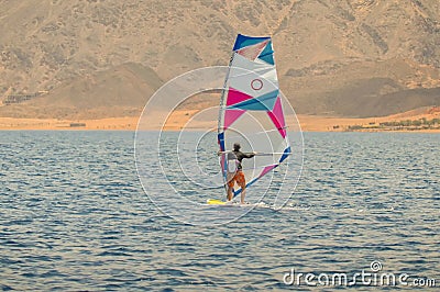 The windsurfer on a board under a sail moves on a calm sea at a low speed, Editorial Stock Photo