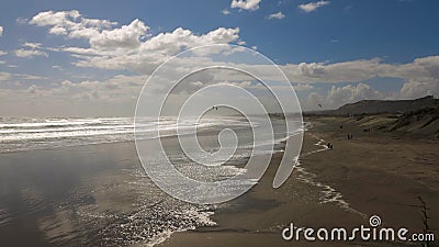 Windy Day on the Wide Brown Sand Beach at Low Tide. Cloudy Sky With the Sun Shining. Small Silhouettes of a Few Walkers Stock Photo