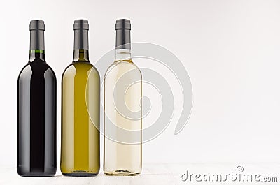 Wine bottles collection different colors - transparent, green, black- on white wooden board, mock up, copy space. Stock Photo