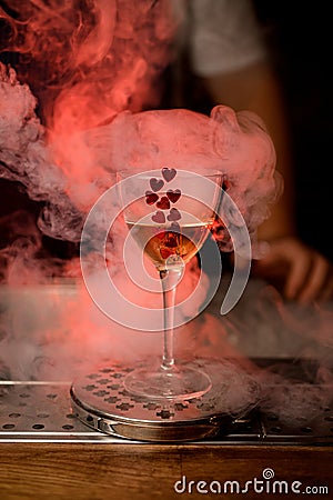 wine glass with drink decorated with red hearts stands on the bar and smoke around Stock Photo