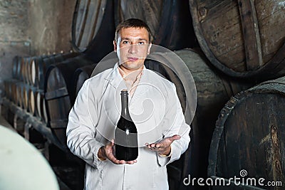 Wine house technician holding bottle near wooden barrels Stock Photo