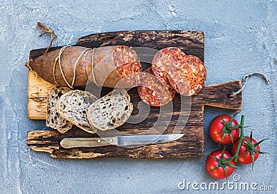 Wine snack set. Hungarian mangalica pork salami sausage, rustic bread and fresh tomatoes on dark wooden board over a Stock Photo